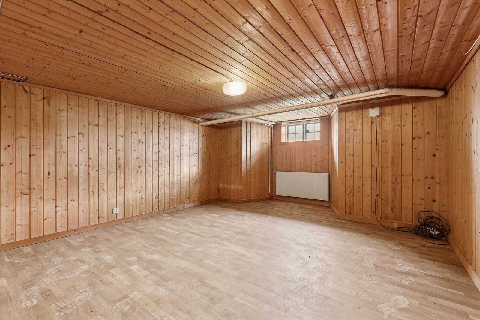 Lyst kjellerrom med panelte overflater og vindu som slipper inn naturlig lys - et areal som enkelt kan tilpasses ulike behov. Galleribilde