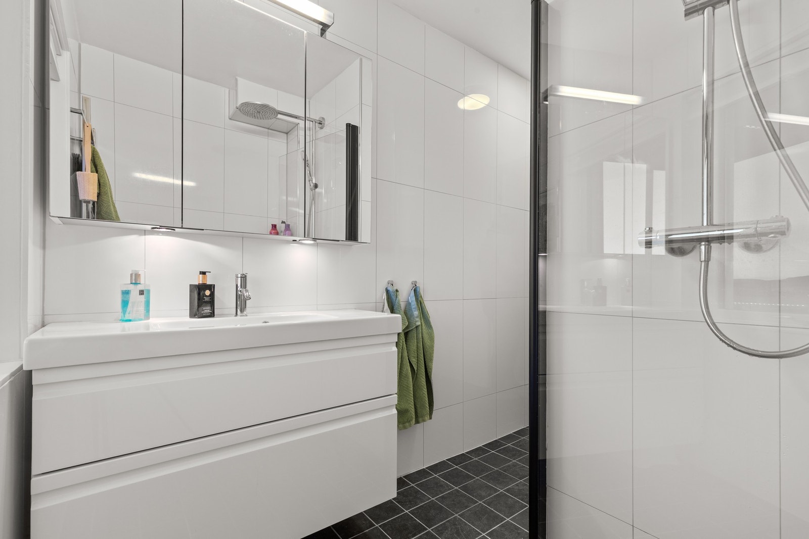 Badet har heldekkende servant med skuffer, speil med belysning samt skap med god oppbevaringsplass. Galleribilde