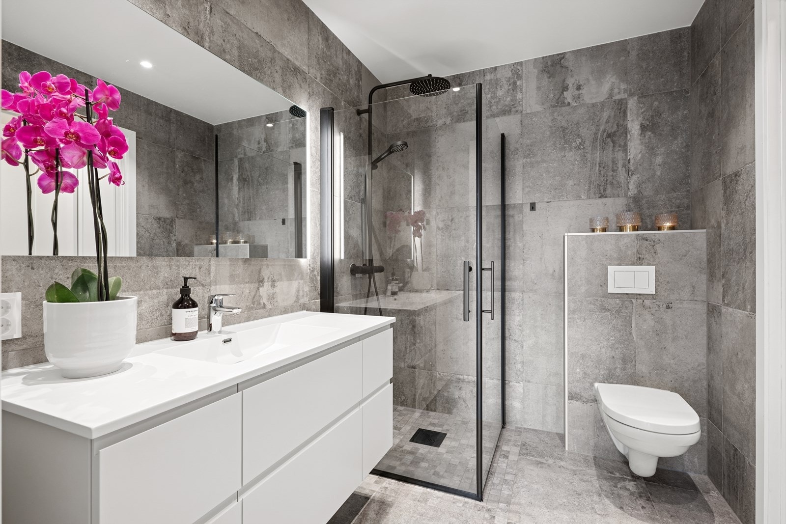 Badet er utført med store fliser på både gulv og vegger - Her finner du vegghengt toalett, dusjhjørne m/glassdører og baderomsinnredning i hvit utførelse Galleribilde