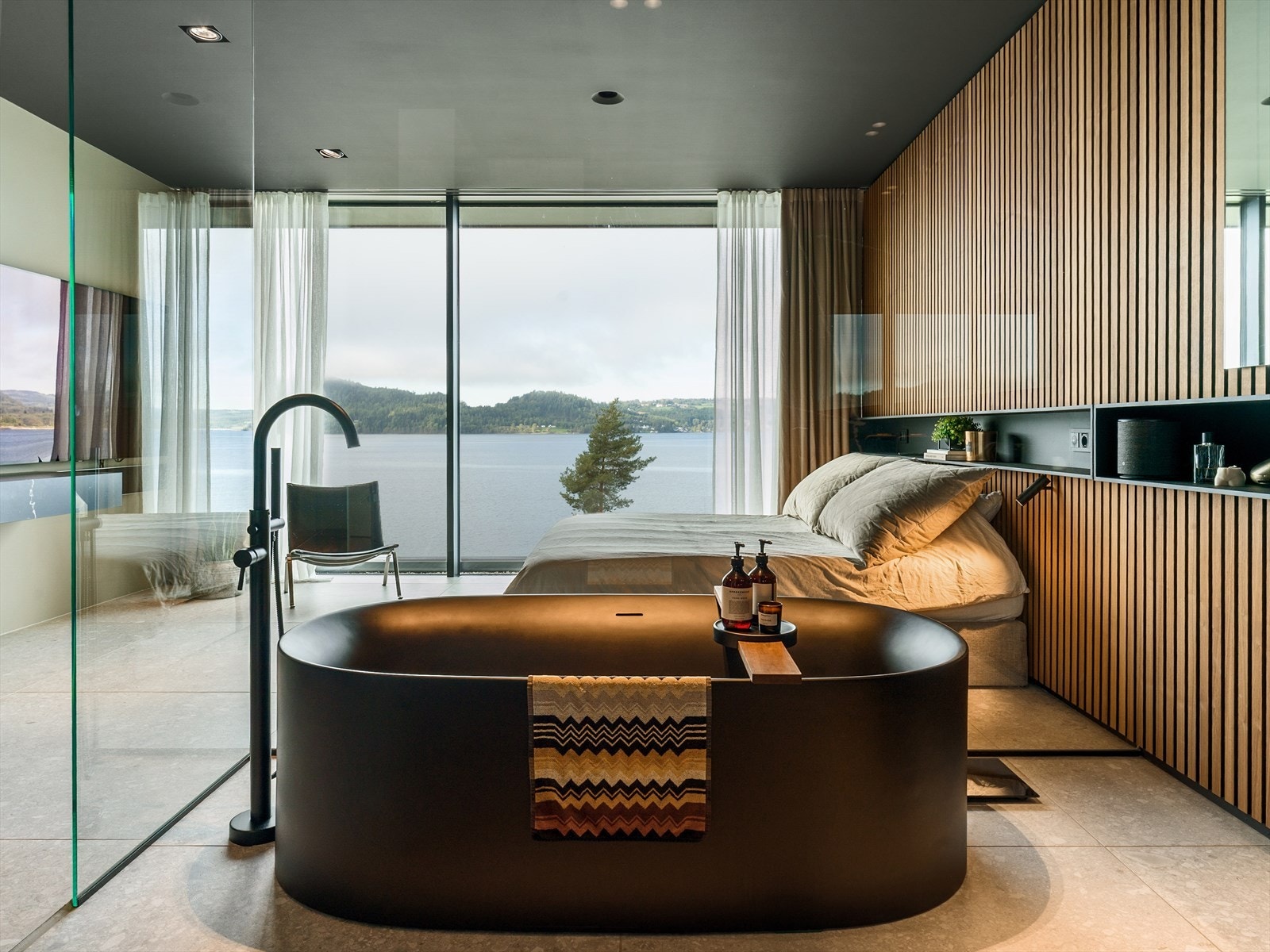 Arkitektonisk eleganse med utsikt - Hovedsoverommet og badet skilles av helglassplater fra gulv til tak, en løsning som gir rommet en åpen, luftig og luksuriøs atmosfære, med Mjøsa som levende bakteppe. Galleribilde