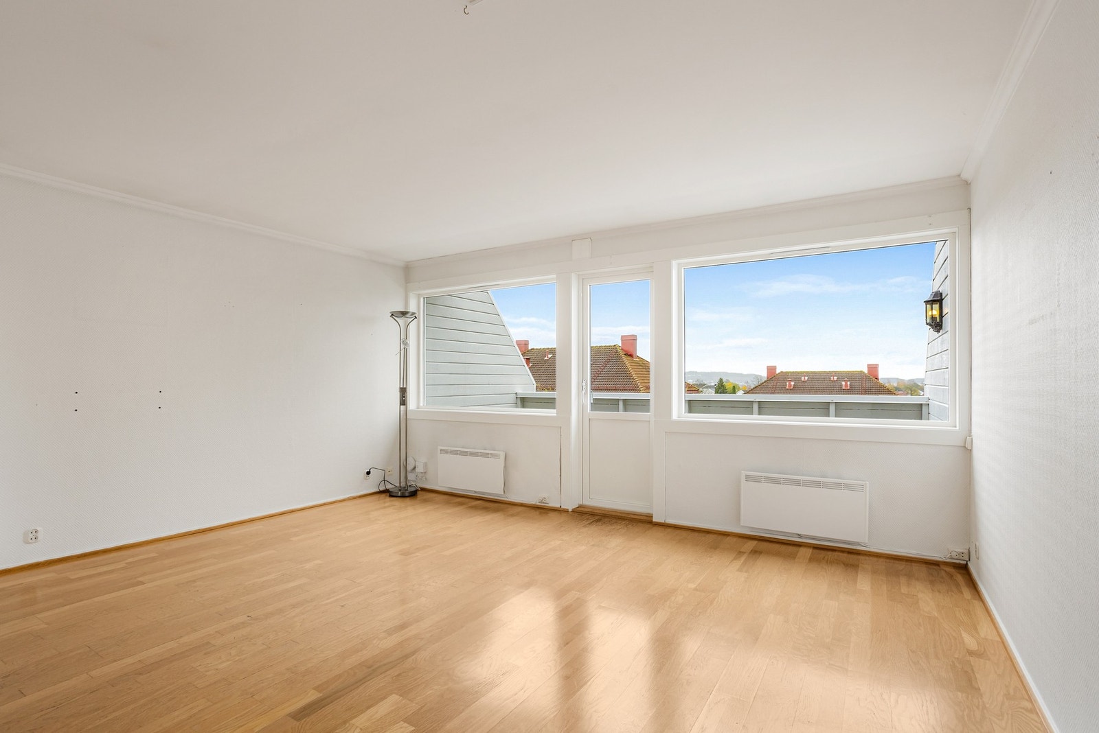 Stuen er et romslig oppholdsrom med parkettgulv, der store vinduer i front slipper inn rikelig med naturlig lys Galleribilde