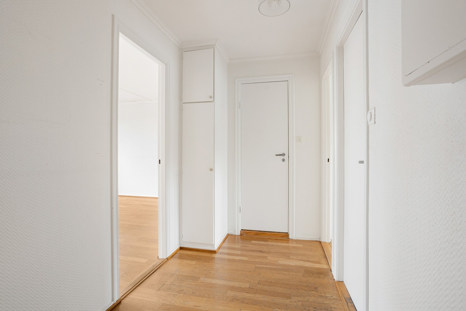 Vel inne har gangen parkettgulv, hvitmalte vegger og et plassbygd garderobeskap Galleribilde