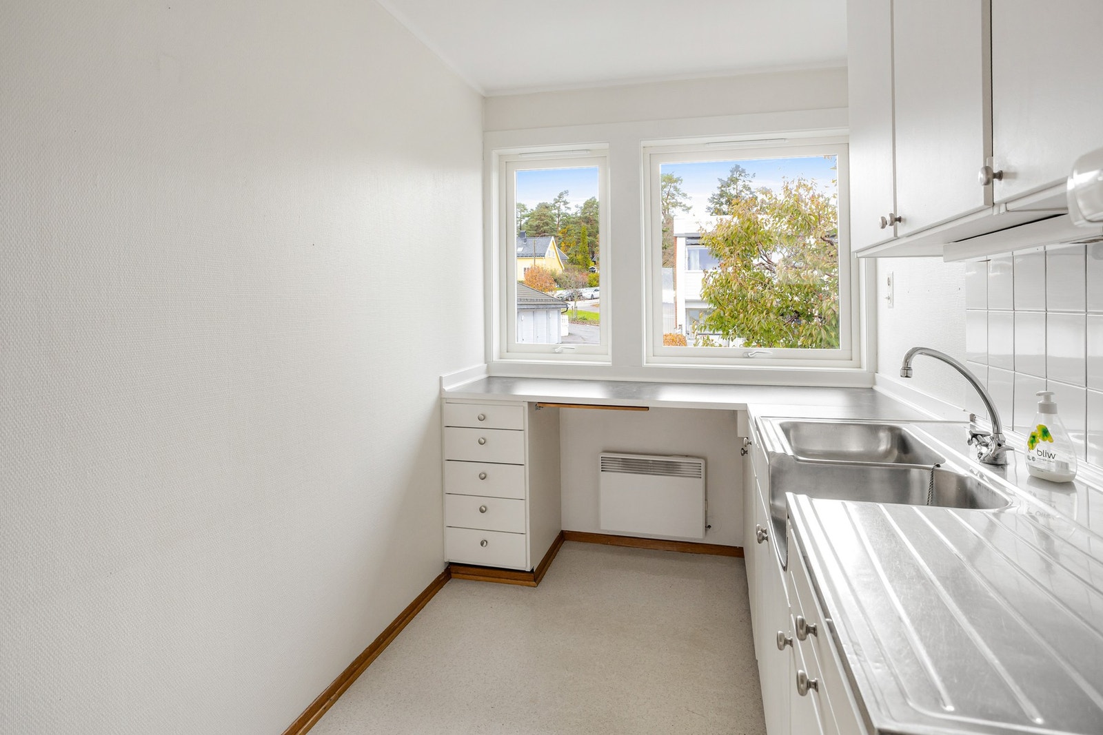 Innredningen er oppført i en funksjonell L-form med hvite, glatte fronter, benkeplate av laminat og dobbel oppvaskkum i rustfritt stål Galleribilde