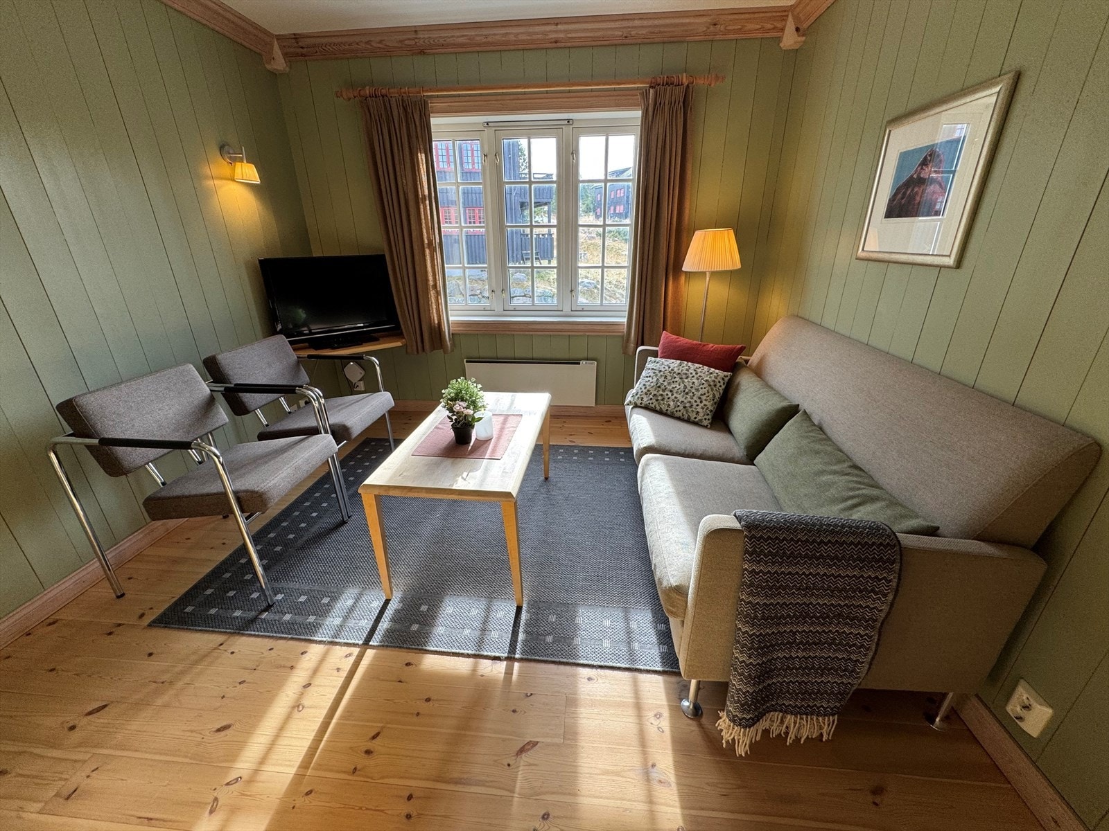 Lys og hyggelig stue med gjennomgående heltre gulv og panelvegger i lune fargetoner. Store vinduer gir godt lysinnslipp og utsyn mot nærområdet. Galleribilde