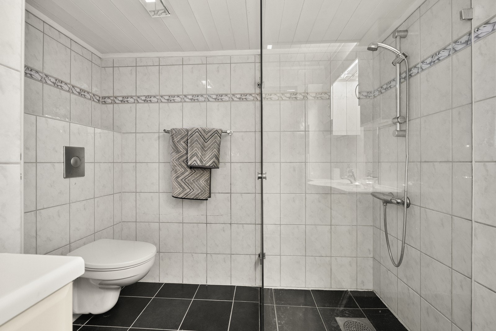Badet er utstyrt med vegghengt toalett, servantinnredning og dusjhjørne med glassvegger. Galleribilde