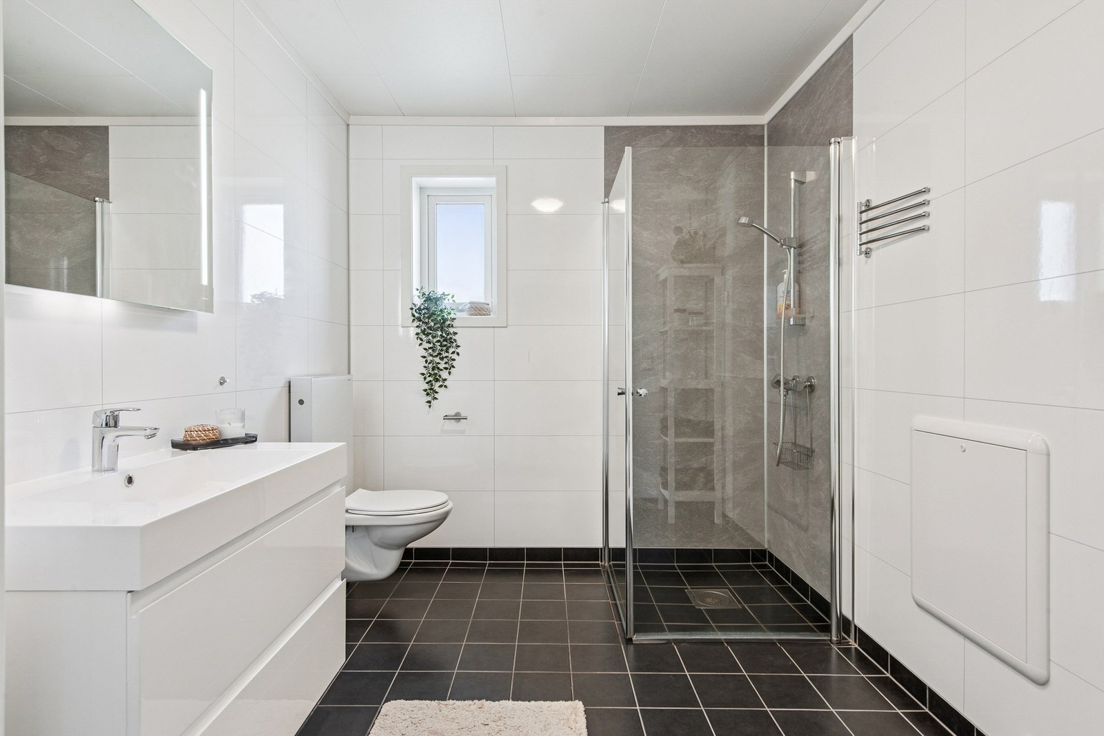 Her er det flislagt gulv med varmekabler, vegghengt toalett og dusjhjørne med innfellbare dører. Galleribilde