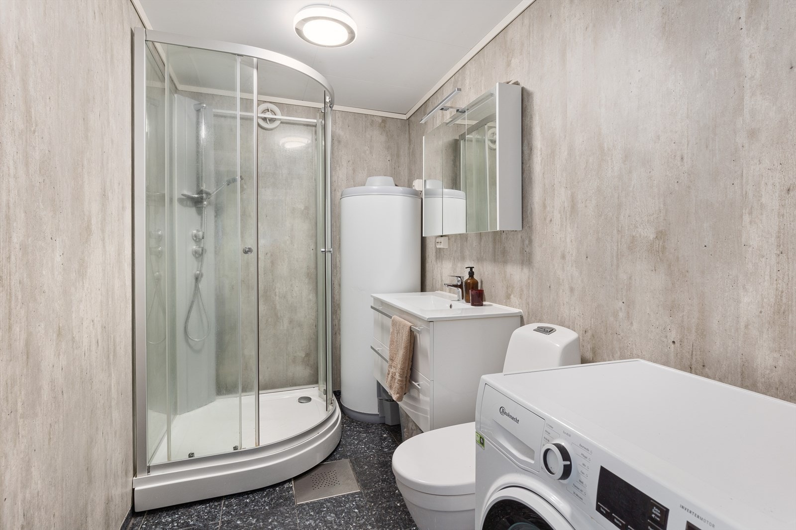 Baderom i hybelen med larvikitt fliser på gulv med varmekabler og baderomsplater på vegger. Innredet med dusjkabinett, stort servantskap og toalett. Galleribilde