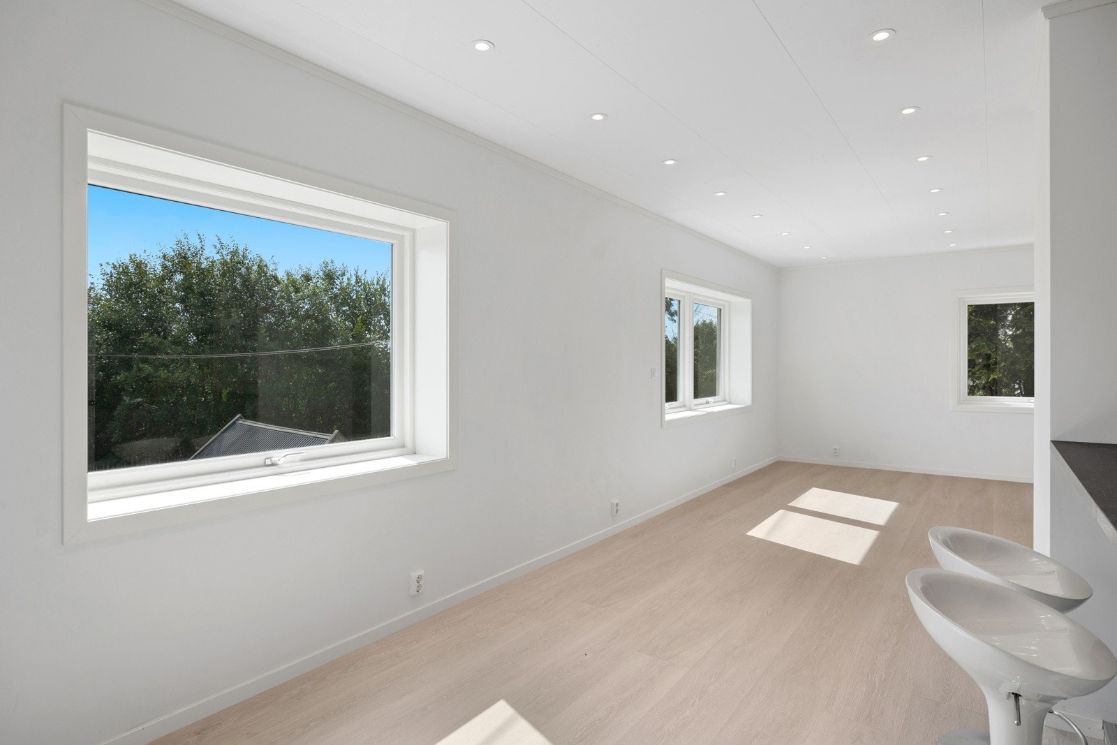 Stor stue med spotter, store vinduer for naturlig lys og panelovner montert i ettertid. Galleribilde