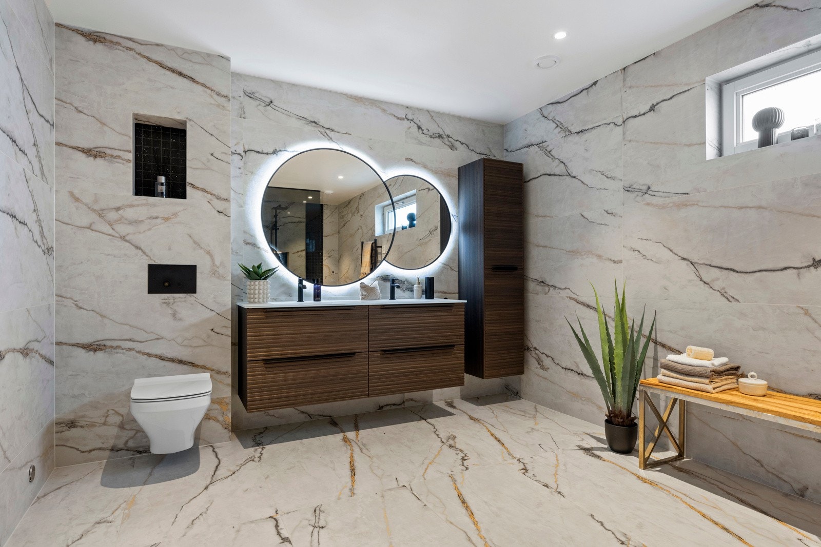 Bad 2 ligger i 2. etasje. Badet har flisagte overflater på gulv og vegger. Badet har veggmontert toalett, veggspeil med integrert belysning, elektrisk håndkletørker, høyskap og baderomsinnredning med finerte fronter og 2 heldekkende servanter. Galleribilde