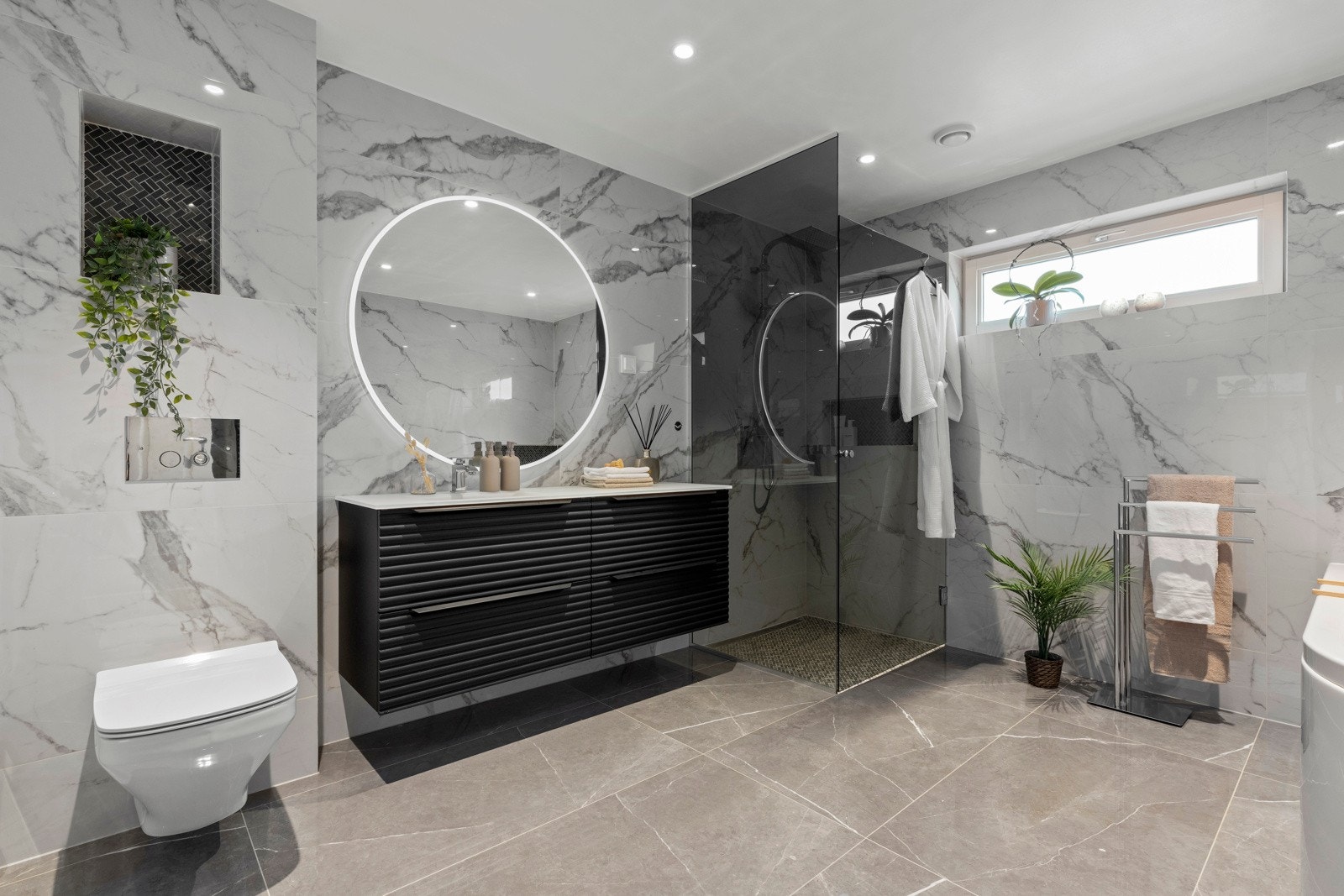 I 1. etasje er det et romslig bad med flislagte flater på gulv og vegger. Badet har veggmontert toalett, dusjvegger i herdet glass, veggspeil med integrert belysning, høyskap med malt front, baderomsinnredning med malte fronter og heldekkende servant. Galleribilde