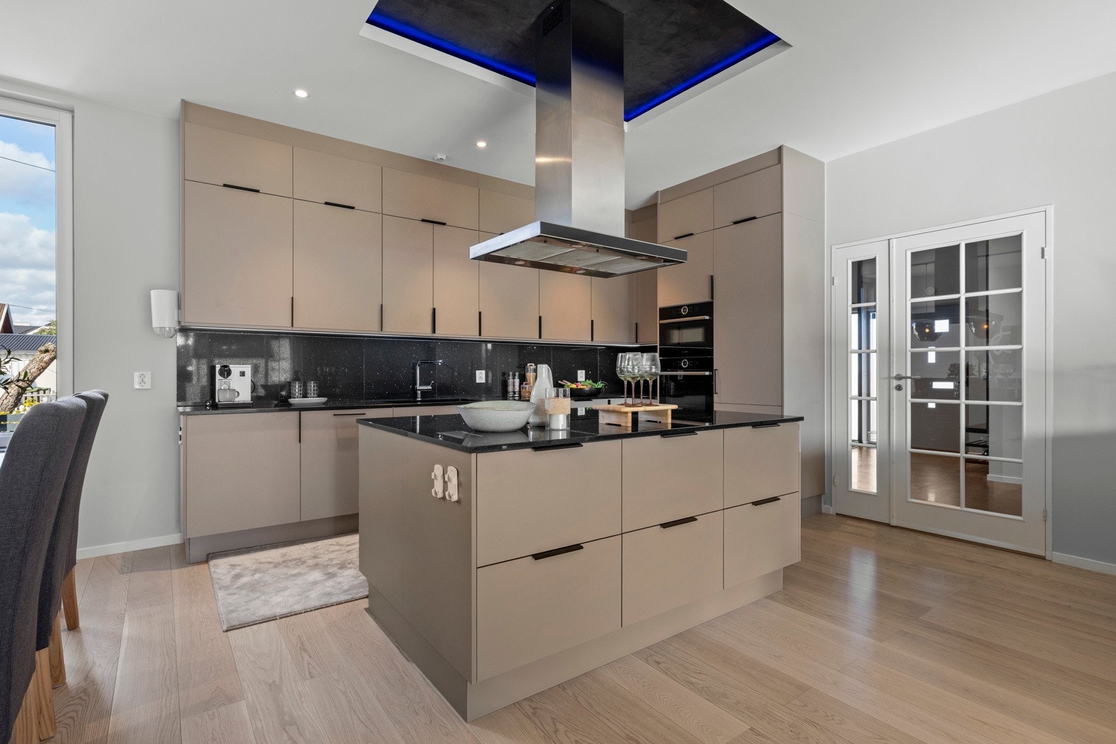 Kjøkkenet har kjøkkeninnredning fra HTH (2021). Innredningen har kjøkkenøy, malte fronter, granitt benkeplater, underlimt oppvaskkum, hetteventilator, granitt over benk og belysning under overskap. Galleribilde