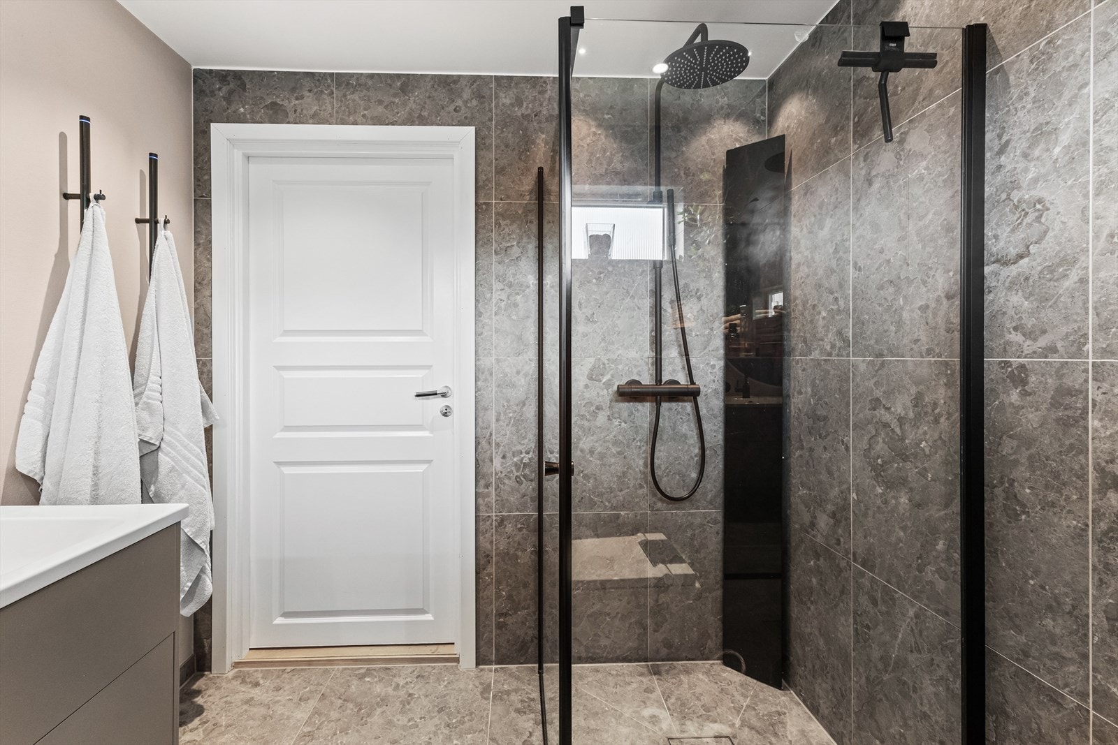 Alt armatur fra Tapwell. Dusjhjørne med regndusj, hånddusj, dusjhylle og glassdører. Elektriske håndkletørkere montert på vegg. Galleribilde