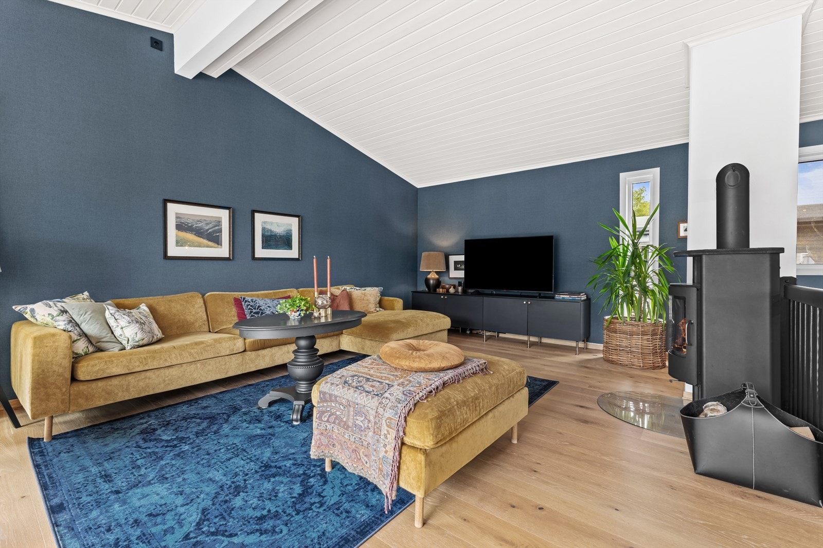 Stue med peisovn fra Rais og god plass til sittegruppe. Hele boligen ble overflateoppusset i 2019 med blant annet tapetserte vegger og ny enstavs eikeparkett. Galleribilde