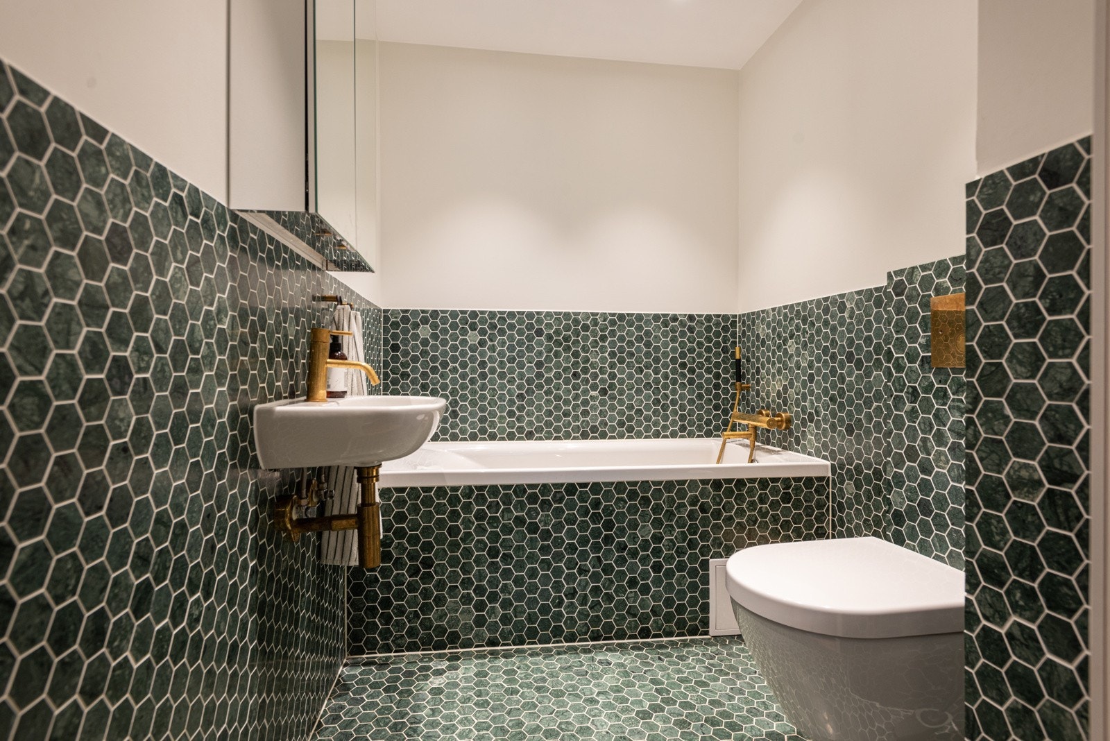 Unikt baderom med grønn marmor flis, innebygd badekar, veggmontert servant og toalett. Galleribilde