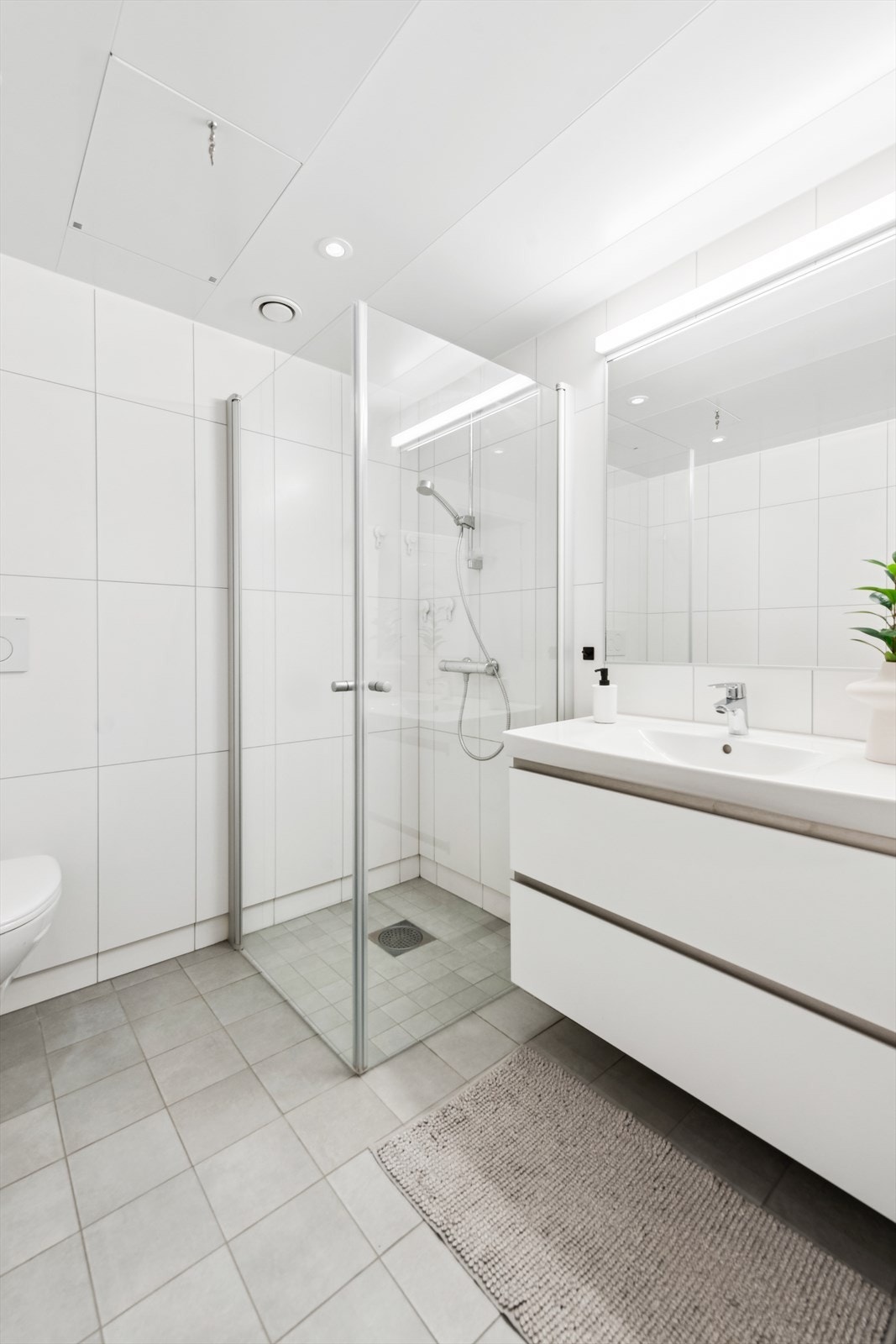 Badet er funksjonelt og moderne med vegghengt toalett, nedfelt servant og dusjhjørne med innfellbare glassvegger. Galleribilde