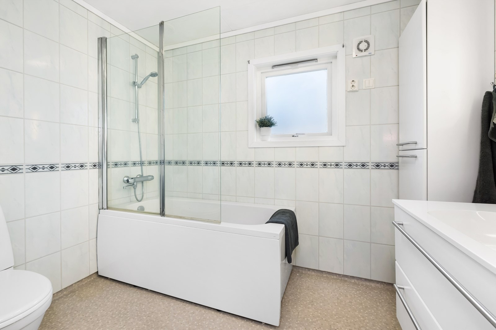 Badet er innredet med gulvmontert toalett, benkeskap med servant og badekar. Galleribilde