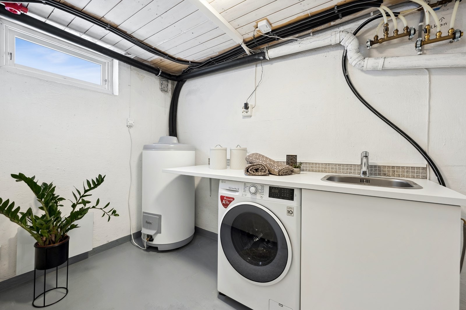 Vaskerom i kjeller med varmtvannsbereder, opplegg for vaskemaskin og arbeidsbenk med vaskekum (bilde er fra forrige salg i 2024) Galleribilde