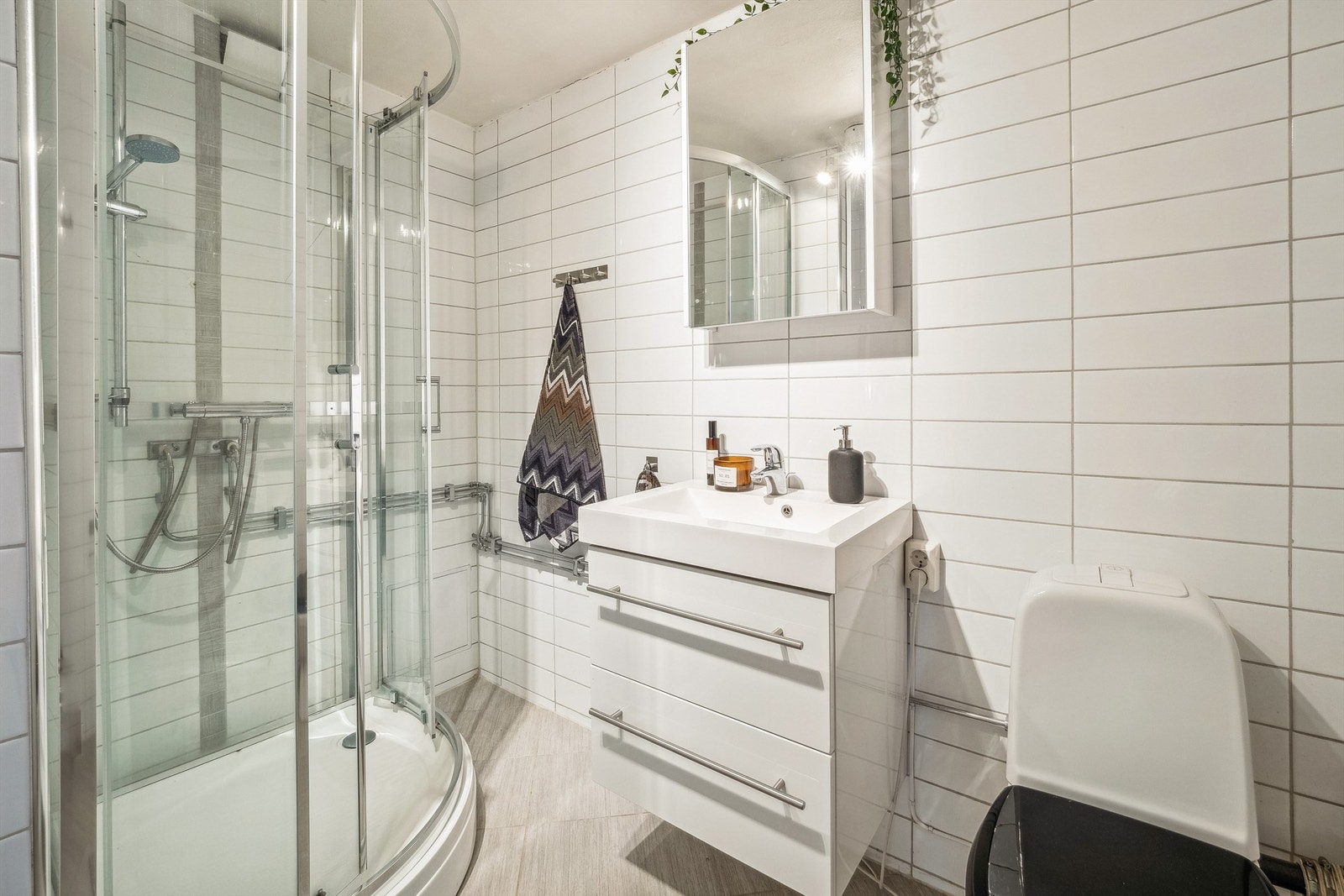 Et baderom har hvite fliser på veggene og lys sandfargede fliser på gulvet. Galleribilde