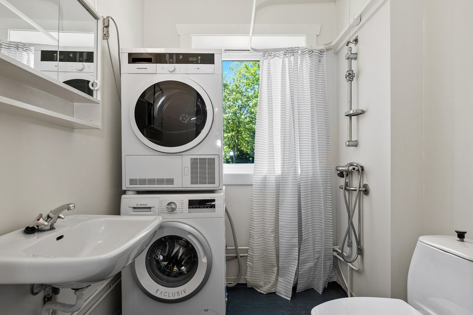 Badet har dusjhjørne med opplegg for vaskemaskin mellom dusj og servant Galleribilde