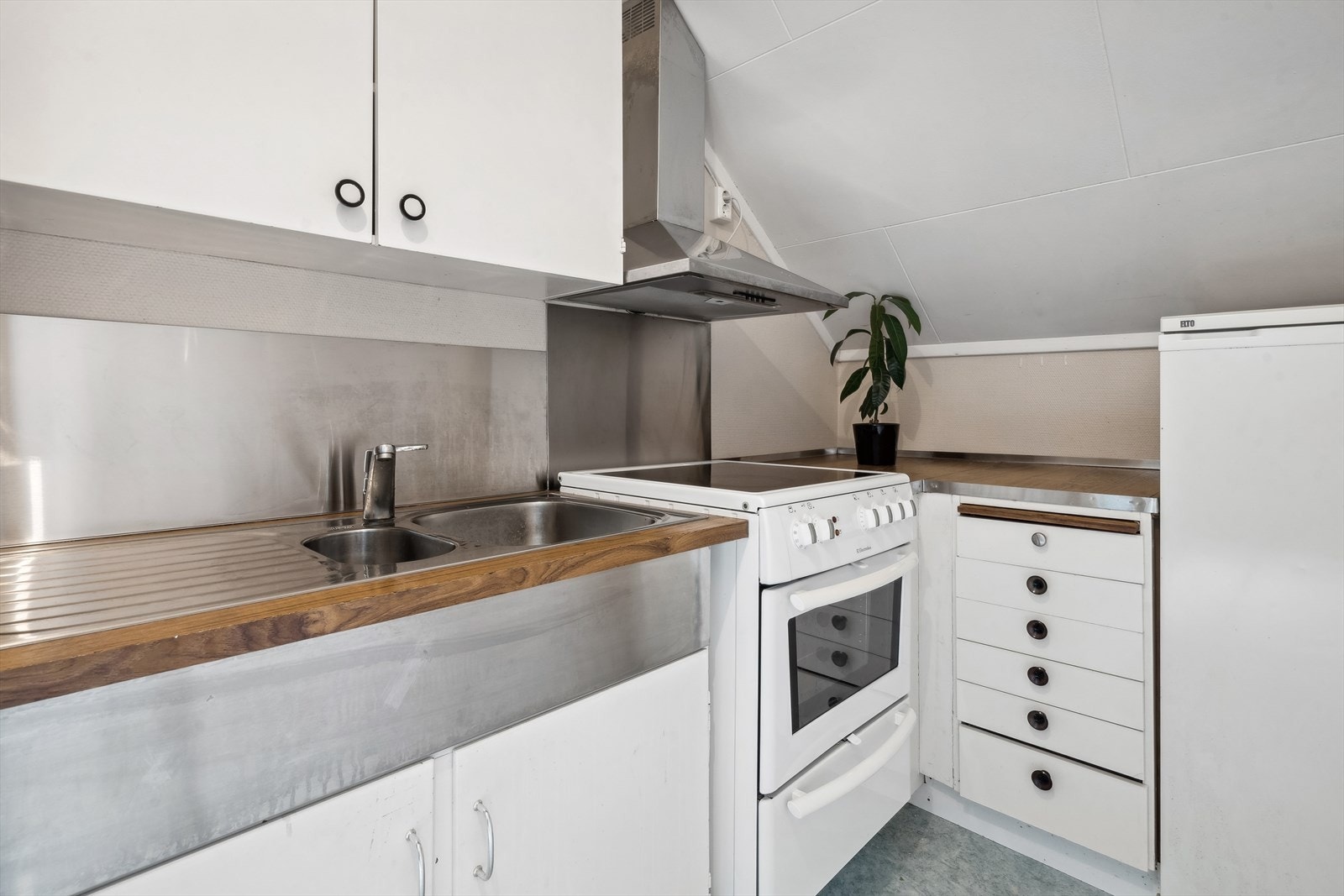 Hybelkjøkken med vinklet innredning og plass til frittstående hvitevarer som komfyr og kjøleskap. Galleribilde