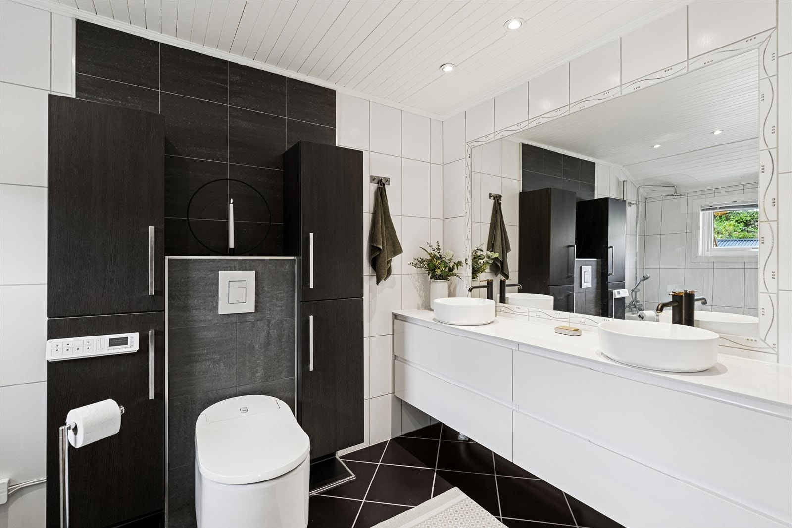 Rommet er innredet med dobbel servant, to vegghengte skap, vegghengt toalett med spylefunksjon og et innbydende badekar - perfekt for avslapning. Det er godt med oppbevaringsplass, og ventilasjonen ivaretas av elektrisk vifte på veggen. Galleribilde