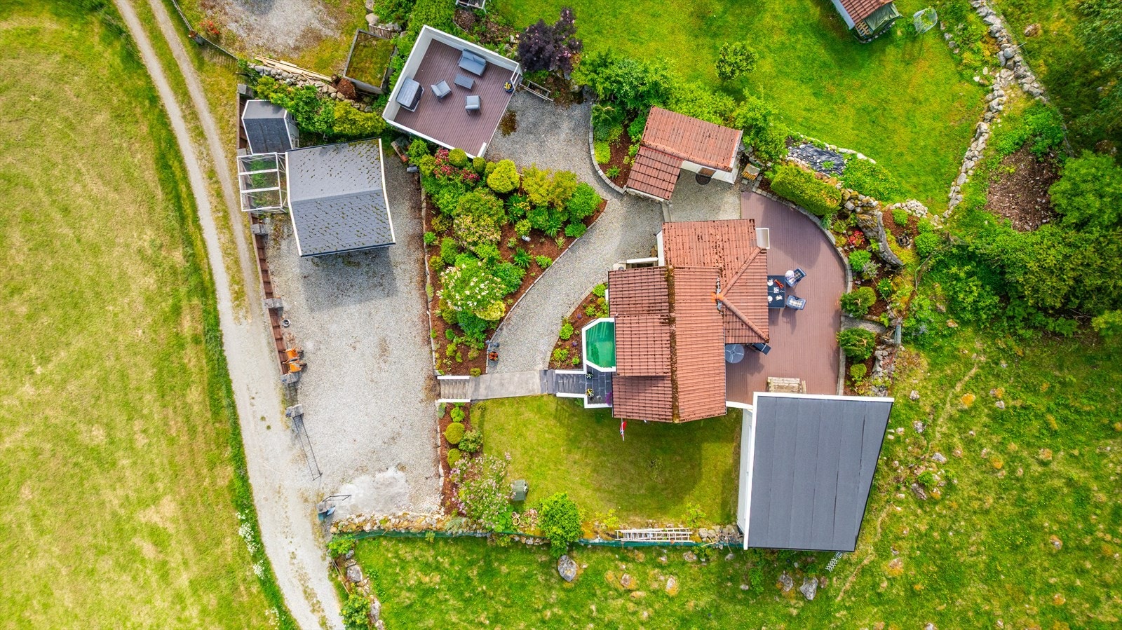 Tomten er skrånende og opparbeidet med terrasse/platting på bakkeplan samt grøntarealer med plen, bed og diverse beplantning. Galleribilde