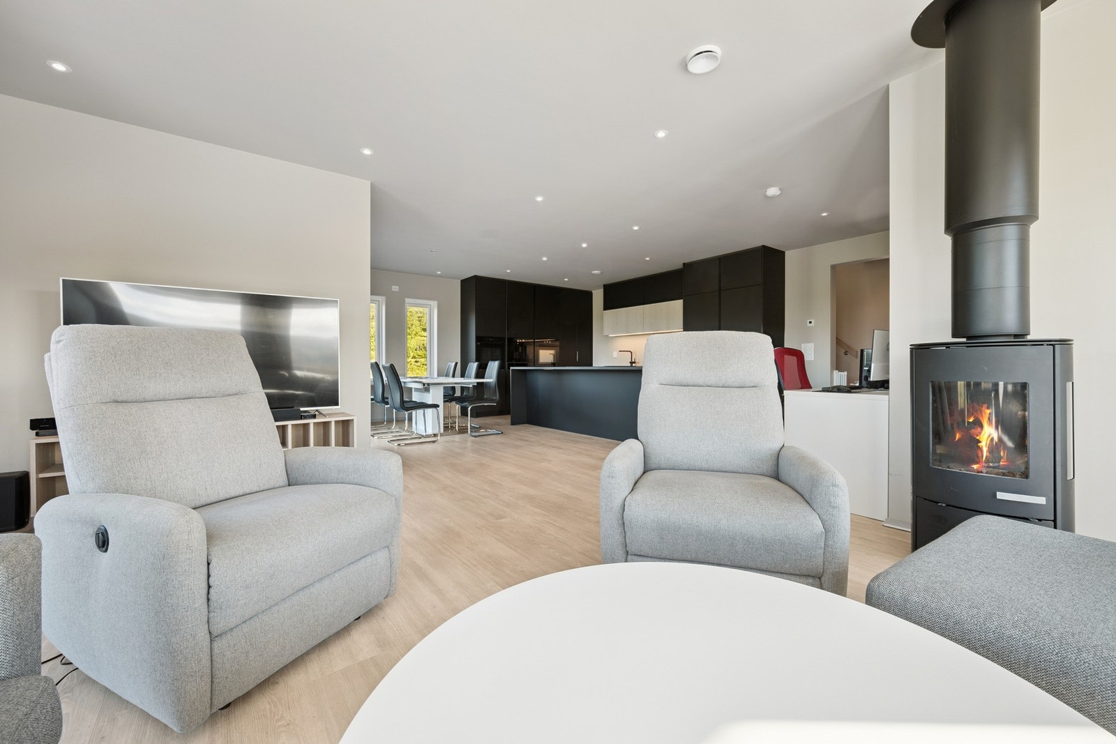Stuen har en moderne vedovn og åpen løsning til kjøkkenet Galleribilde
