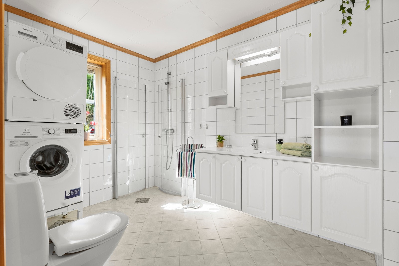 Lyst bad med dusjhjørne - praktisk innredet med toalett, servant og opplegg for vaskemaskin/tørketrommel. Galleribilde