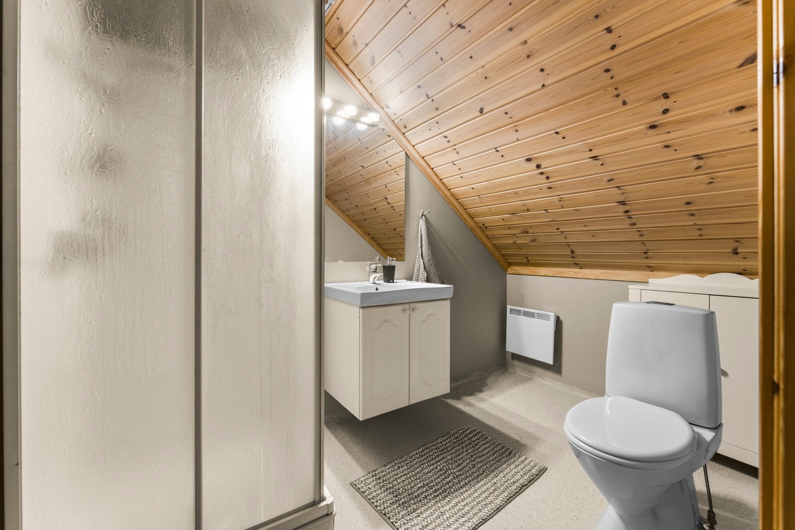 Lyst og funksjonelt bad med dusjkabinett, gulvmontert toalett og innredning med nedsenket servant og speil. Overflatene er enkle å holde rene, og rommet byr på en praktisk planløsning som gjør det velegnet til både daglig bruk og gjester. Galleribilde