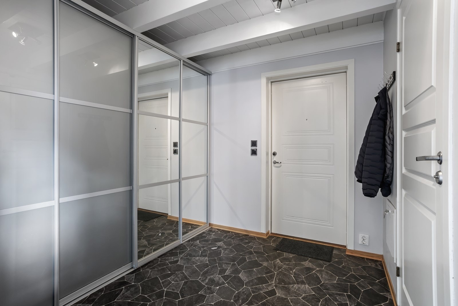 Velkommen inn til entréen med plass til oppheng av yttertøy og til å sette ifra seg sko. Her finner du et stilrent garderobeskap med skyvedører, som tilbyr rikelig med oppbevaringsplass. Galleribilde