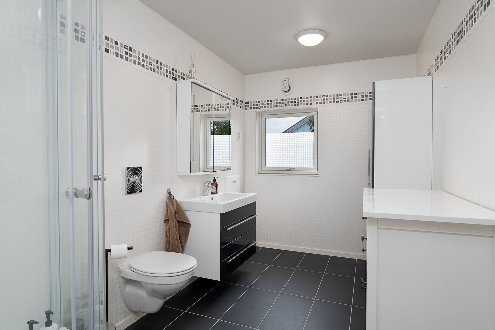 Bad/vaskerom i leilighet 2 med våtromsbelegg på vegg, slettmalt gips i himling og flislagt gulv med elektriske varmekabler. Innredning med servant, høyskap, speilskap, toalett, dusjkabinett, samt opplegg for vaskemaskin. Galleribilde