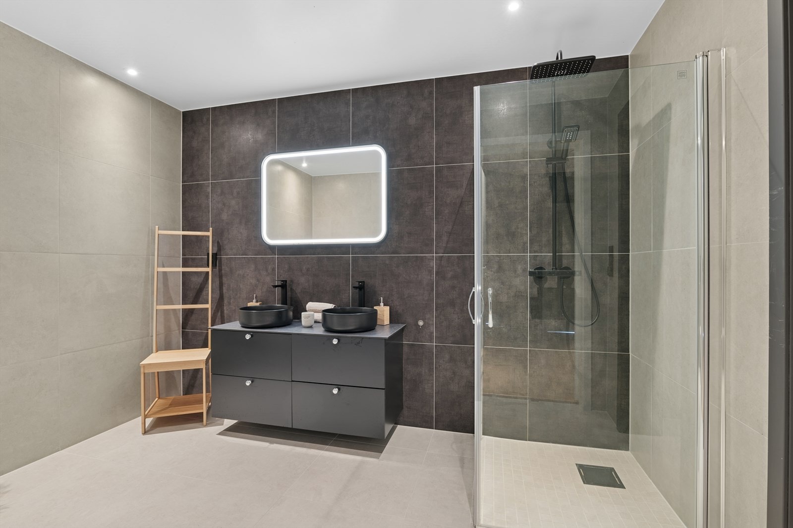 Badet har en lekker og moderne gjennomførelse med flislagt gulv og vegger i 60 x 60 cm, med behagelige gulvvarme. Det er pene kontraster og sømløse overganger mellom vegg- og gulvflisene. Galleribilde