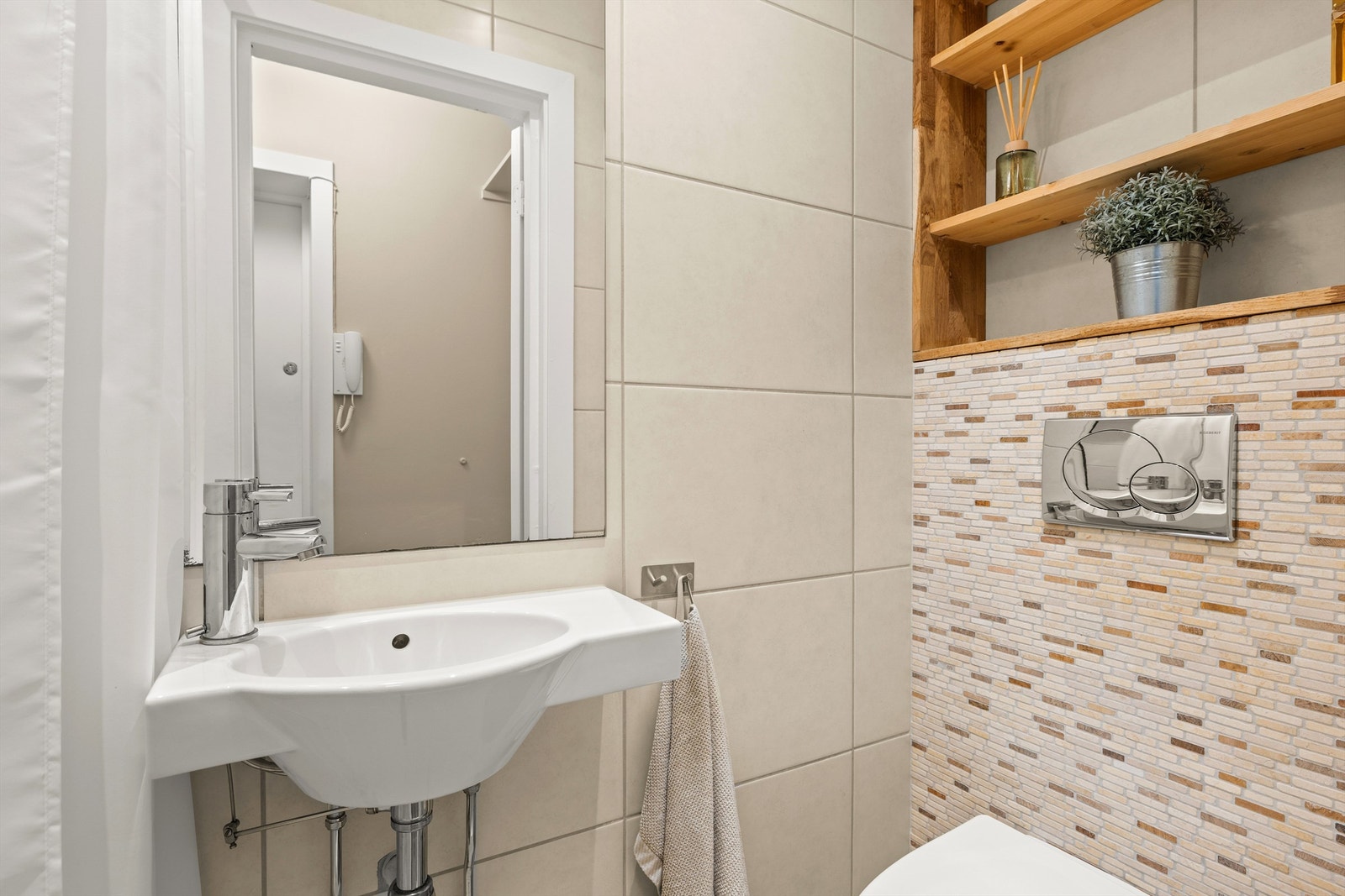 Badet er flislagt og innredet med vegghengt toalett og servant. Galleribilde