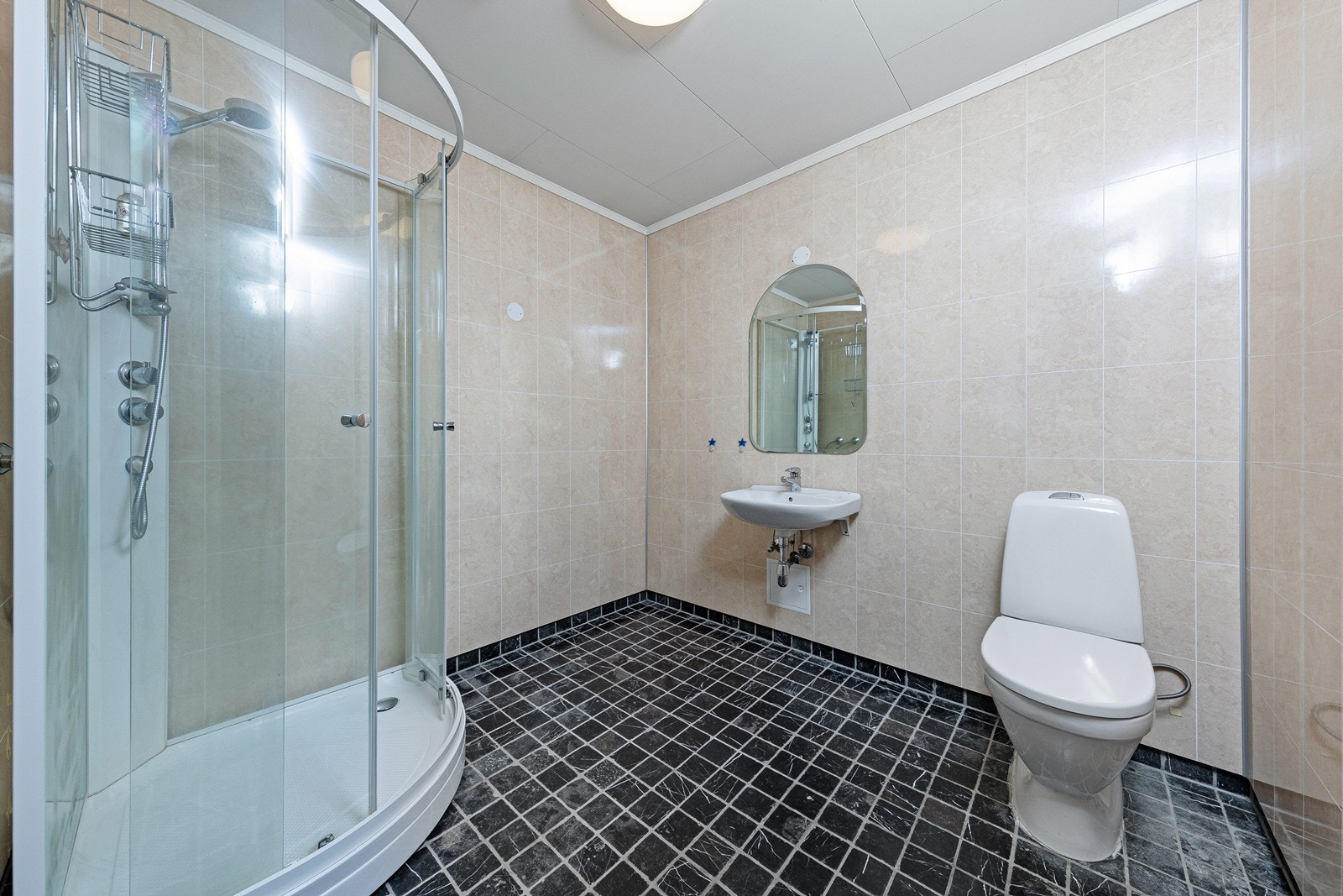 Badet er av eldre standard med baderomsplater på veggene og himlingsplater i taket. Rommet er utstyrt med servant, toalett og dusjkabinett. Galleribilde