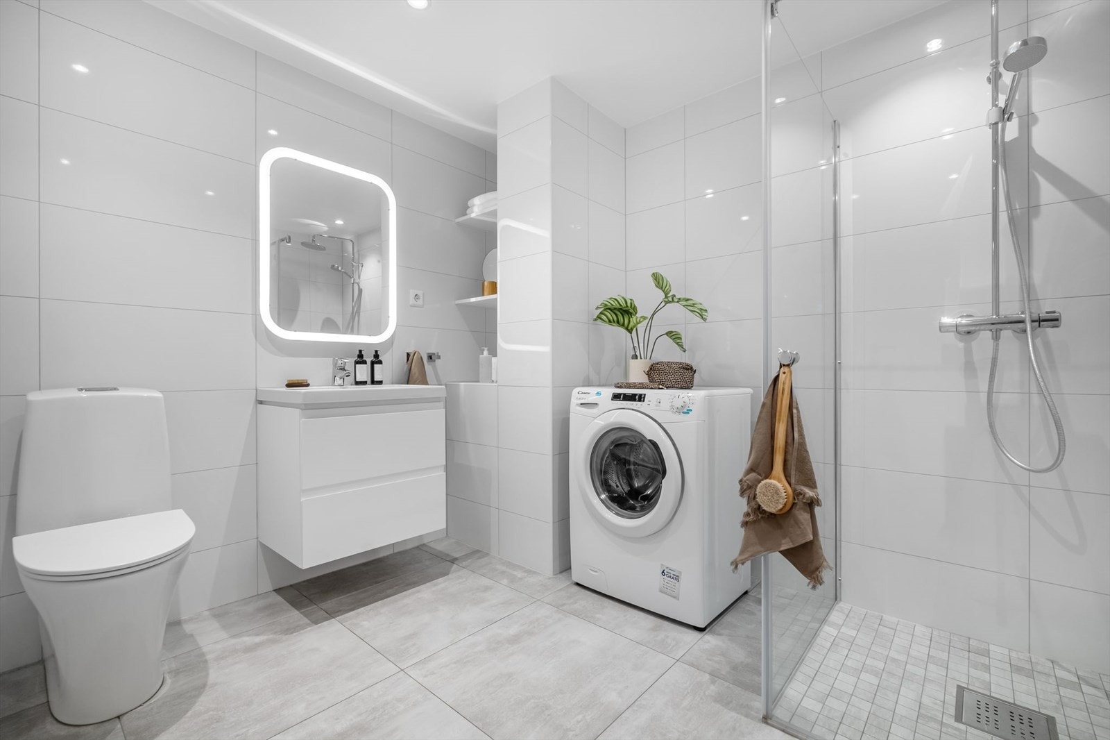 Flislagt baderom med downlights og malt overflate i himling. Rommet har gulvvarme. Videre er det utstyrt med dusjhjørne, mekanisk avtrekk, opplegg for vaskemaskin, servantskap, servant og wc. Galleribilde