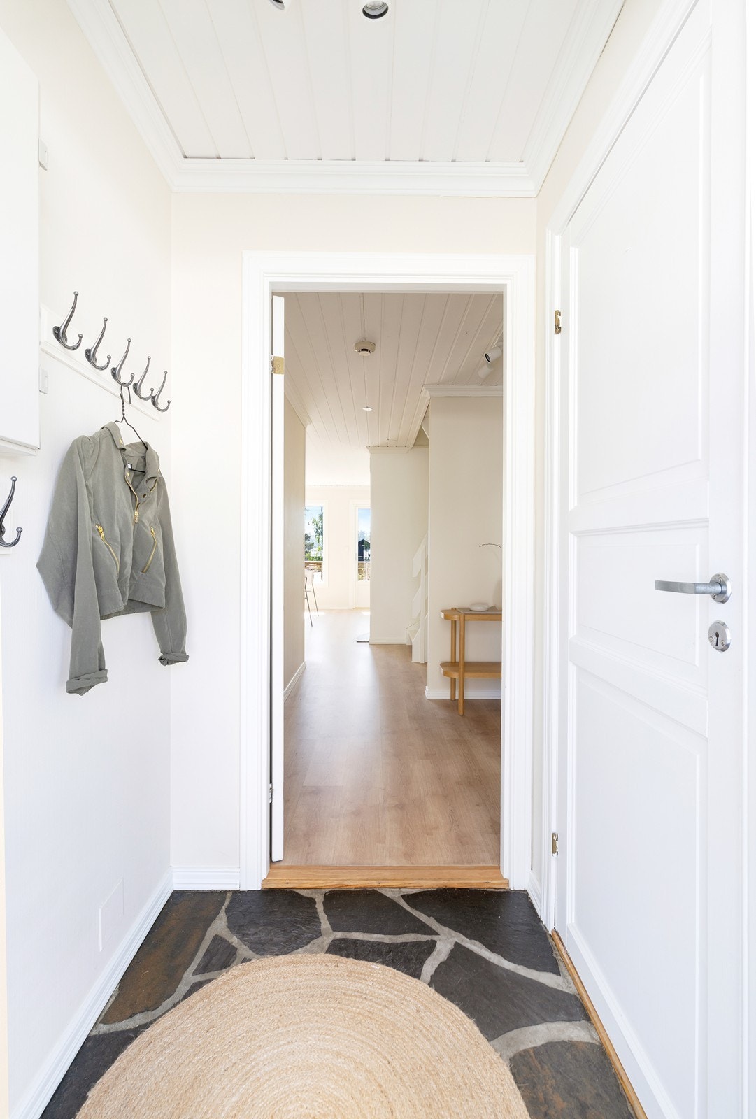 Gang med skiferfliser på gulv. Plass til å henge av seg ytterklær og sko. Inngang til gjestetoalett. Galleribilde