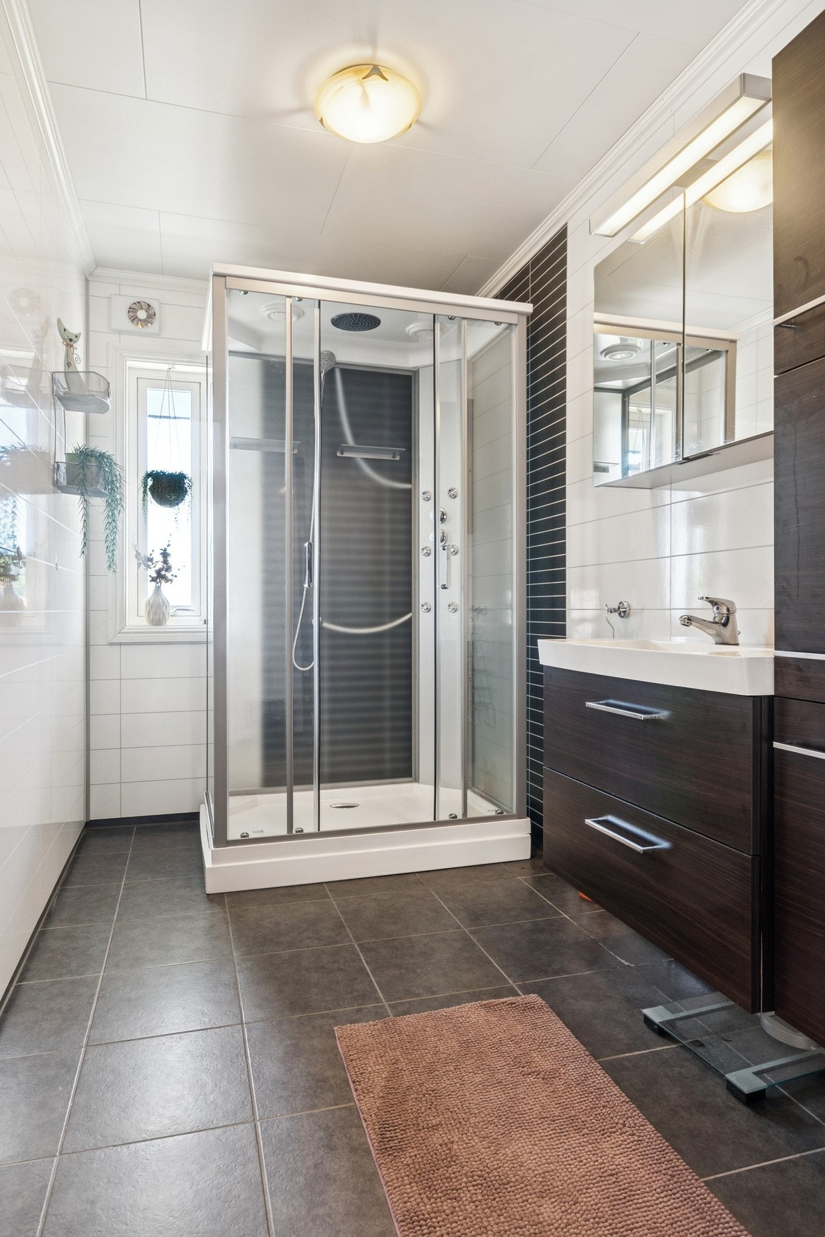 Badet har flislagt gulv med elektriske varmekabler, og våtromsplater på vegg. Det ble pusset opp i 2012, og dusjkabinettet er fra 2025. Galleribilde