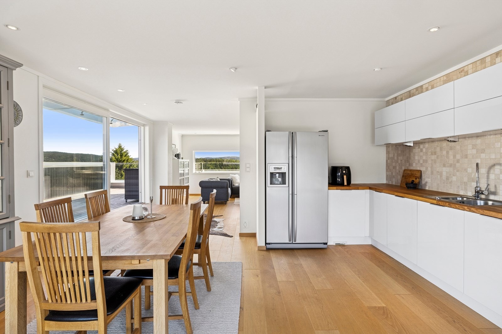 Kjøkkenet har en stilren innredning med fronter i hvit høyglans og benkeplate av tre med nedfelt kjøkkenkum. Galleribilde