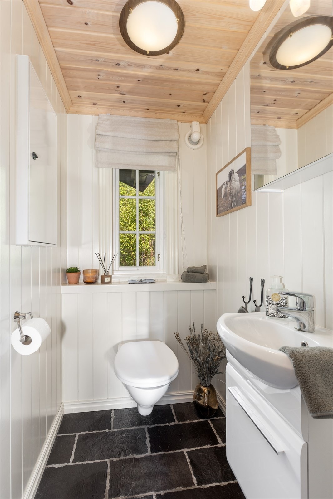 Hytta har eget toalettrom hvor det også er flislagt gulv med varmekabler og malt mdf-panel på vegger. Her er det enkel servant med underskap og speilskap med overlys. Veggmontert toalett og avtrekksvifte på yttervegg. Galleribilde