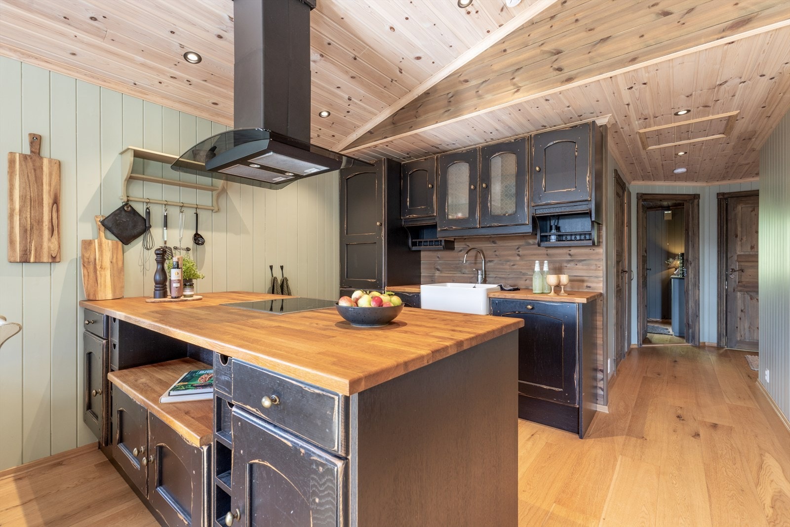 Kjøkkenet har et fint skille mot spisestua med kjøkkenhalvøy hvor det er oppbevaringsplass på begge sider. Her er det spesiallaget innredning fra Huseby av sort aldringsmalt massiv eik med plass til alt man måtte trenge på hytta. Galleribilde
