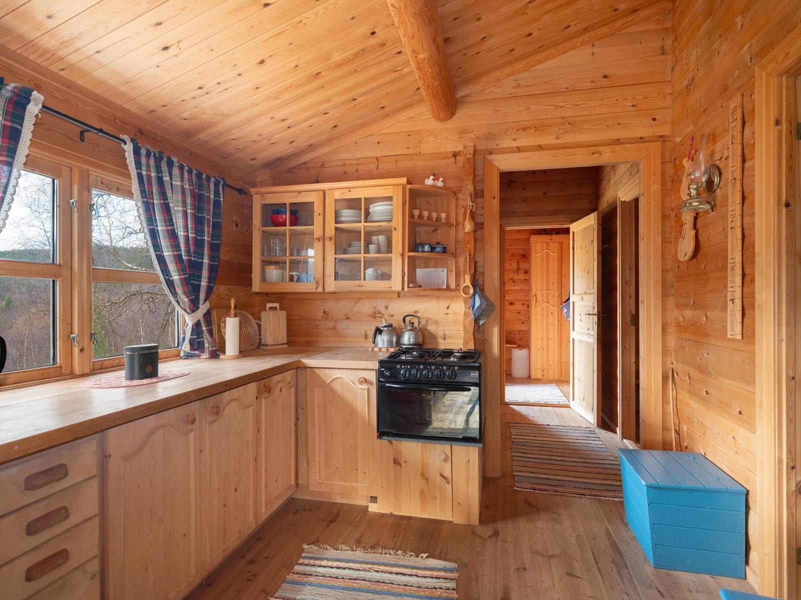 Tregulv og tømmerplank på vegger. Panel i himling. Gasskomfyr, kjøleskap og vedovn Galleribilde