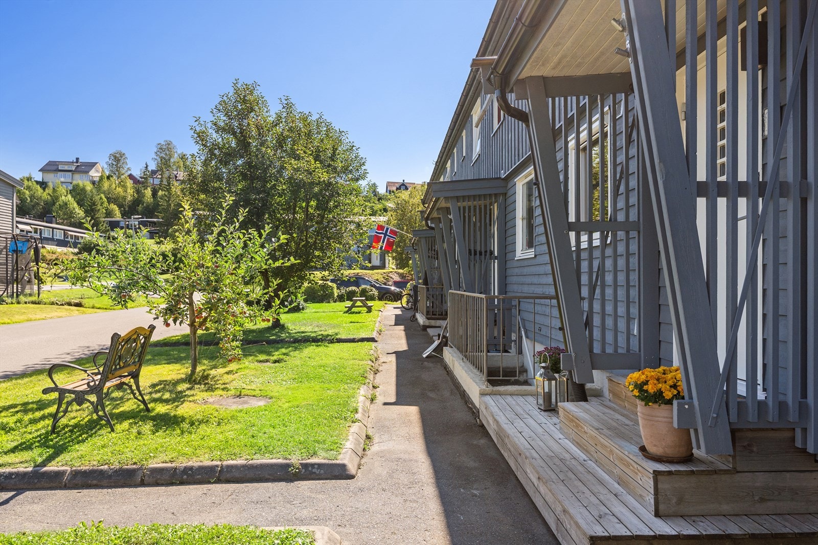 Hyggelig område utenfor inngangspartiene til rekken. Her er det plener, sitteplasser og pent beplantet med trær og busker. Ned trappen har du en praktisk inngang til vaskerom i underetasjen. Galleribilde
