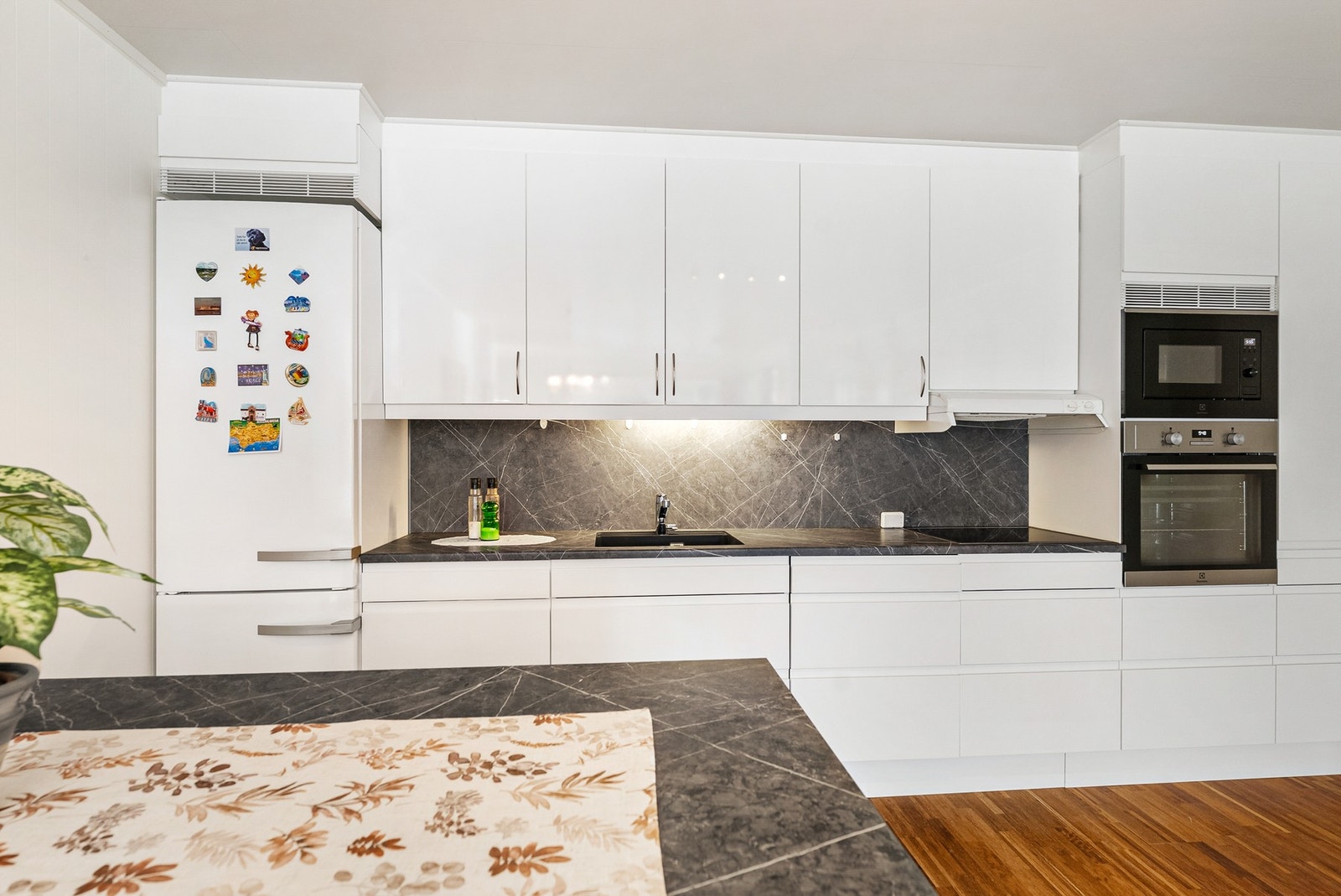 Innredningen har glatte, hvite fronter og er godt utnyttet med både benkeskap og overskap, som gir rikelig oppbevaringsplass og et rent, moderne uttrykk. Galleribilde