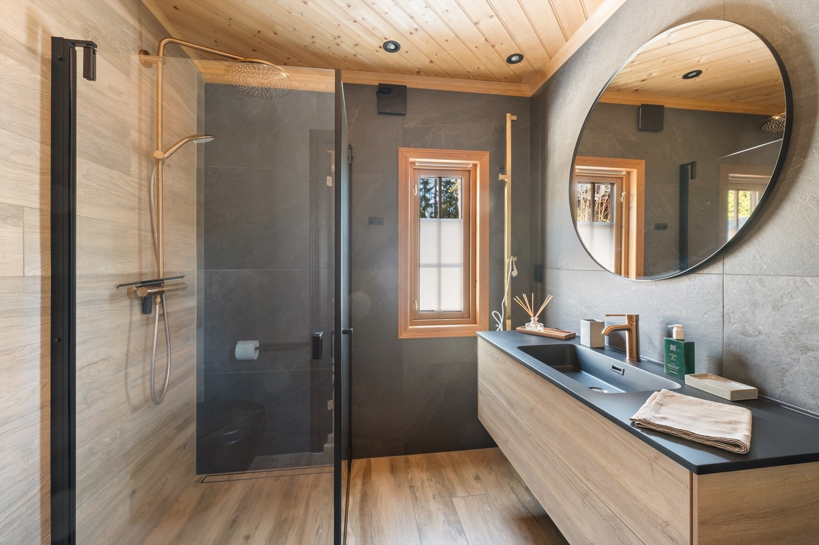 Lekkert baderom med et gjennomført og eksklusivt uttrykk. Det er dusjhjørne med gullfarget regnfallsdusj, vegghengt servantinnredning og gullfarget håndklestativ. Galleribilde