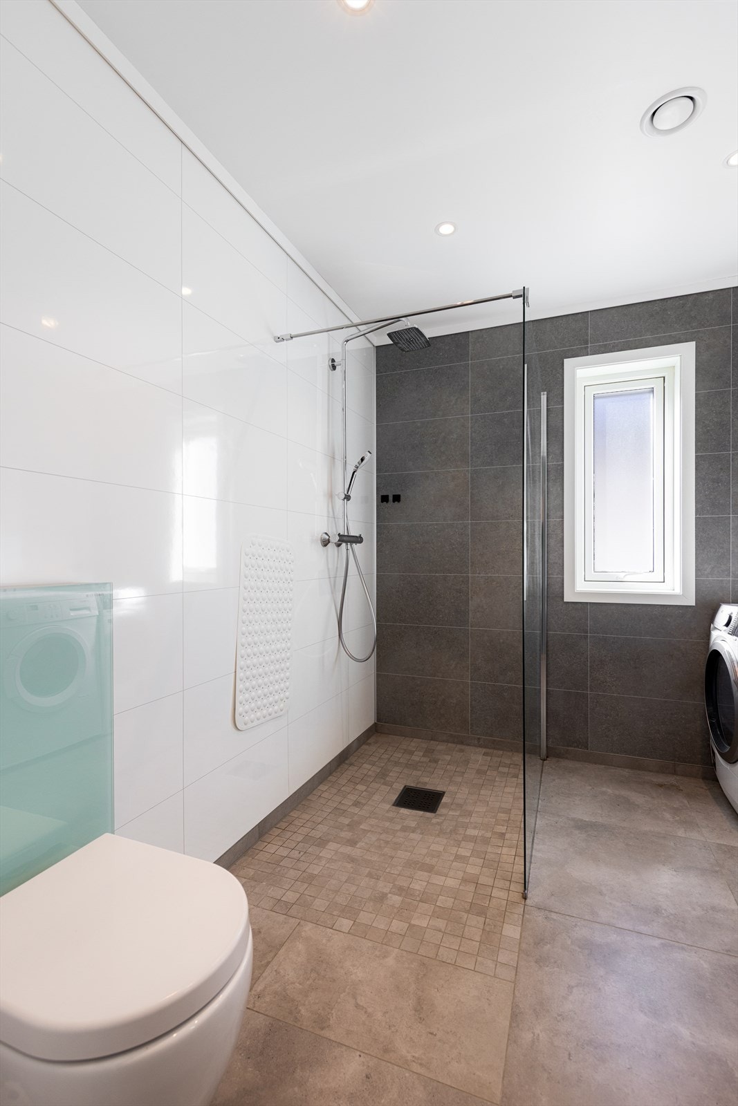 Badet har flis på gulv med varmekabler, baderomsplater på vegg og malte gipsplater i tak med spotter. Galleribilde