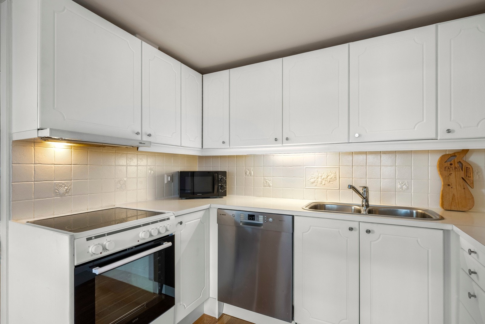 Kjøkken med laminatbenkeplate, integrert oppvaskmaskin, frittstående komfyr og kjøleskap med fryser. Galleribilde