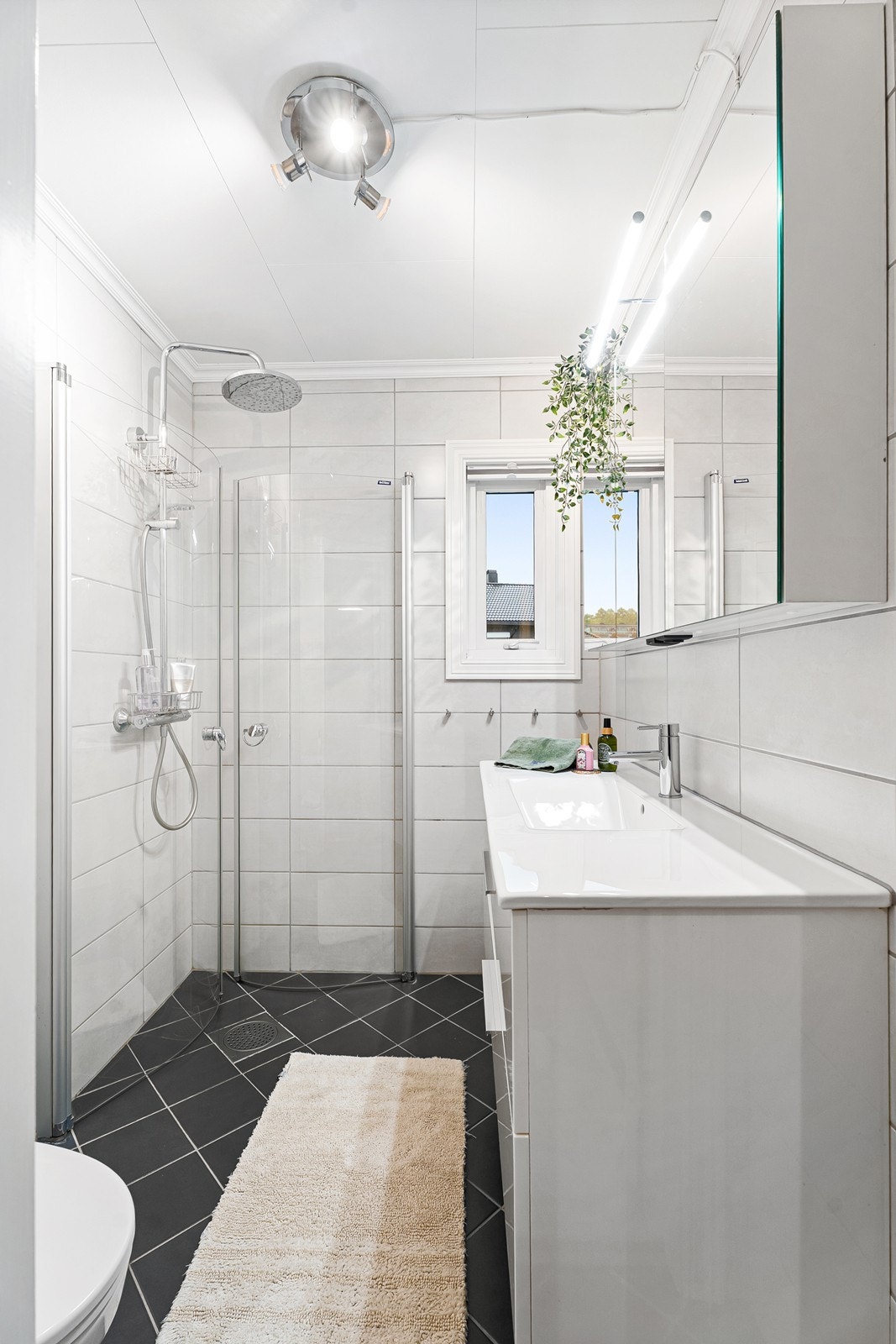 Badet i denne etasjen er helfliset i tidløse fliser med dusjhjørne, vegghengt toalett og flott innredning med speil og oppbevaring. Galleribilde