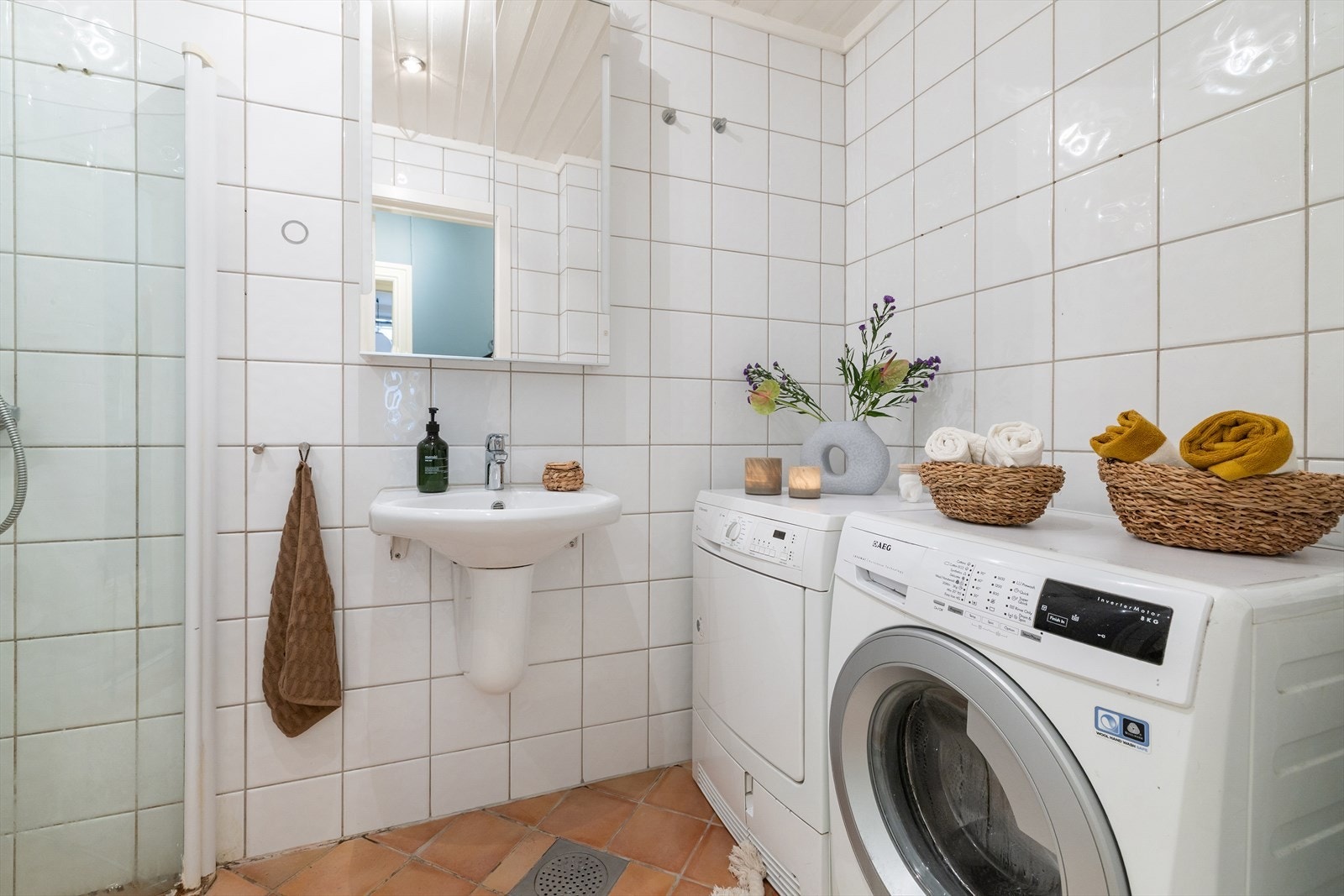 Praktisk, tidløst bad med flislagte overflater, gulvvarme og malt panel med downlights. Det er opplegg for vaskemaskin. Galleribilde