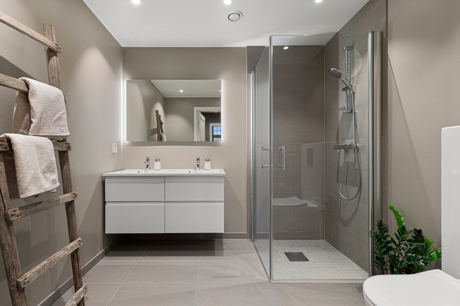 Lekkert bad med malte plater på vegger og flislagt gulv med varmekabler. Innredningen er bestående av vegghengt klosett, dusjnisje og baderomsinnredning med doble servanter og speil Galleribilde