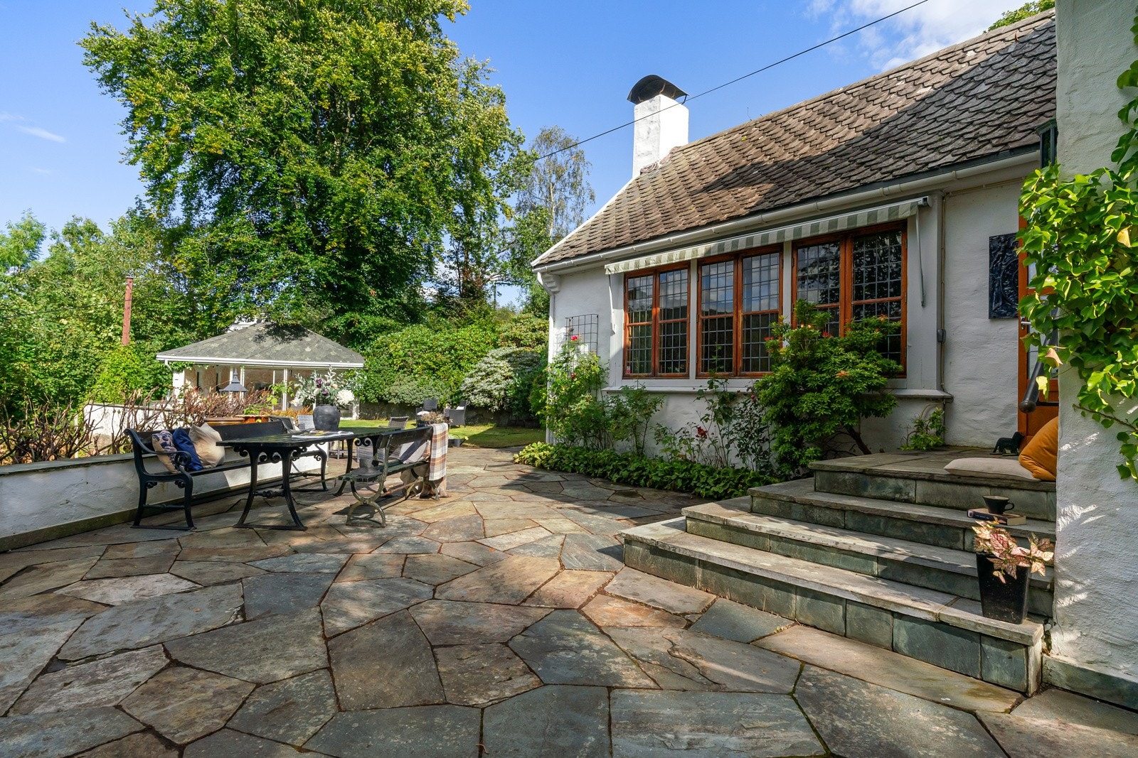 Deler av hageområdet er belagt med skifer, som komplementerer husets særtrekk. Legg merke til de nydelige teak-vinduene med blyinnfattet glass. Galleribilde